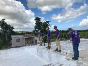 4 volunteers spreading sealant onto a large roof with the puerto rico sky in the background