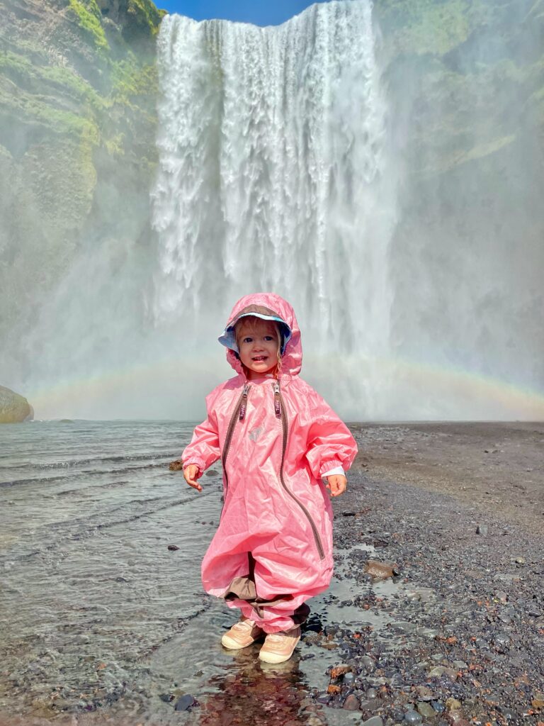 Toddler in pink rain suit in front of Skogafoss Waterfall Iceland