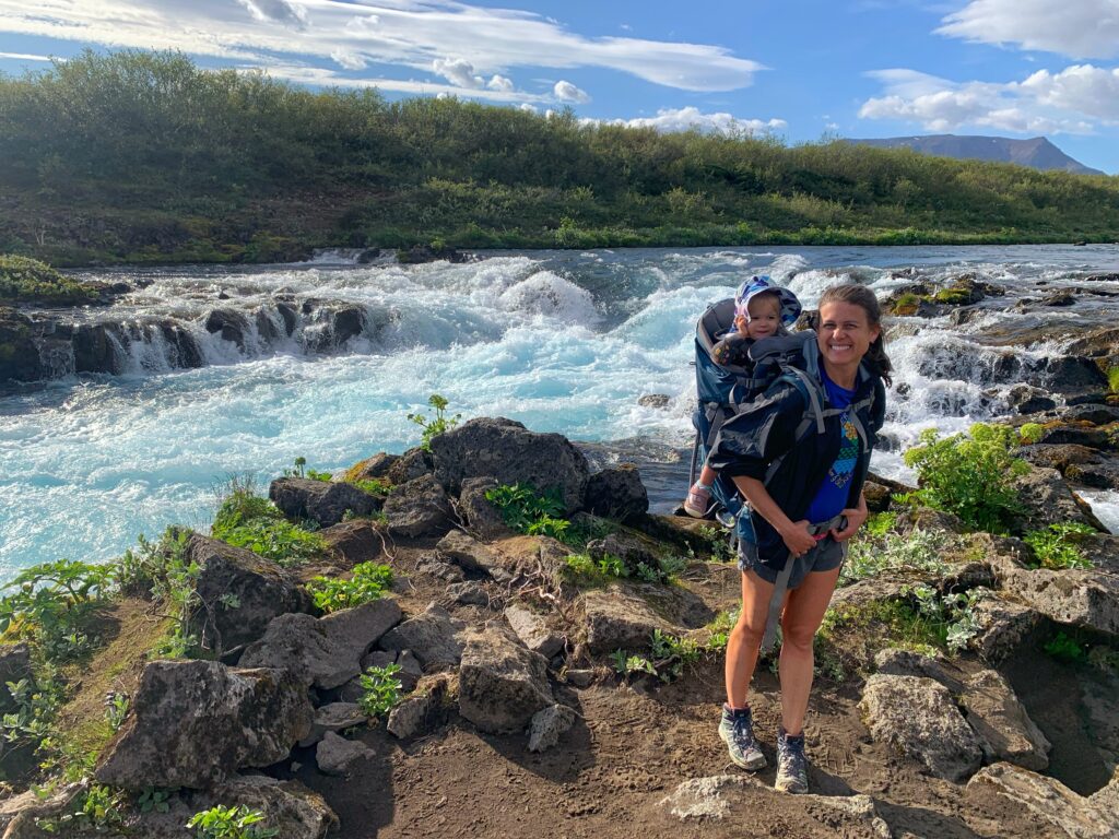 hiking by blue waterfall in Iceland with toddler in hiking carrier